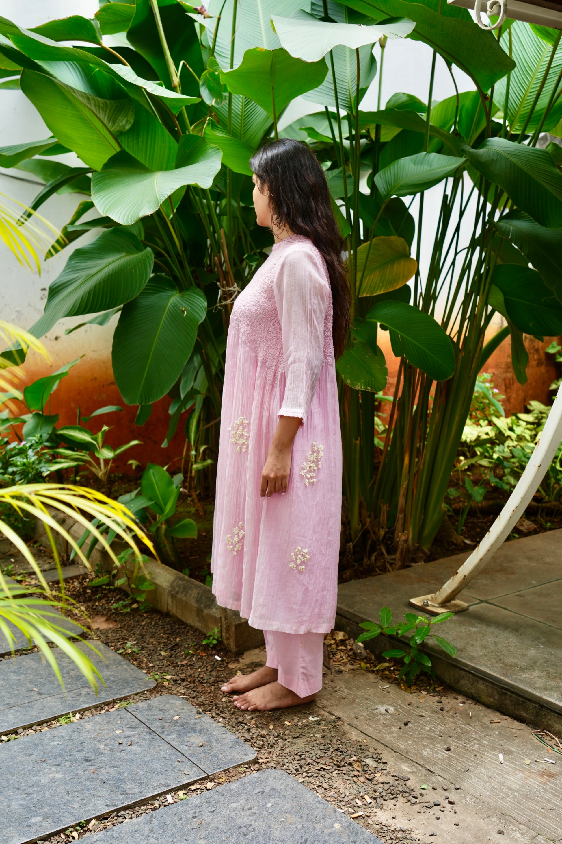 Woman in a pink outfit standing among lush green plants